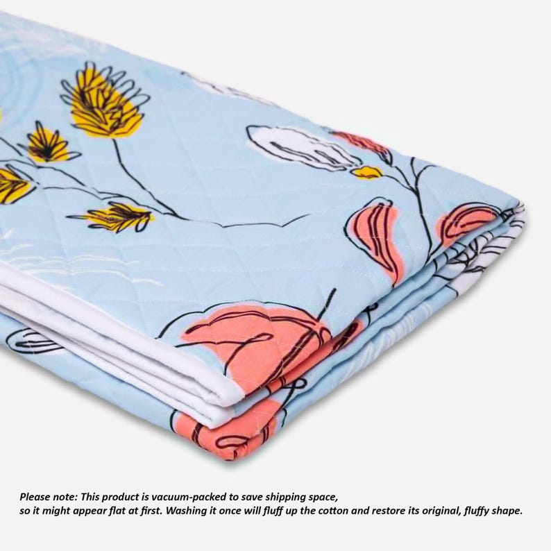 May include: A light blue quilted blanket featuring a printed pattern of stylized yellow flowers and coral-colored leaves with thin black outlines. The fabric has a diamond-stitched texture and white edges, folded to show multiple layers of the material.