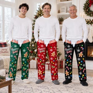 May include: Three pairs of holiday pajama pants in green, red, and black, each featuring a white long-sleeve shirt, a graphic of a gingerbread man, candy canes, Christmas lights, snowflakes, and the text Frosty Buns with a white faux-fur trim.