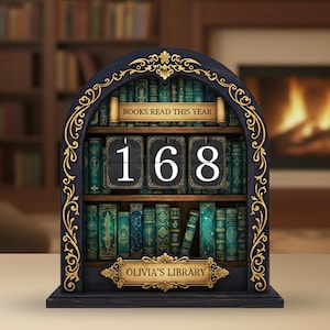 May include: A dark blue wooden bookshelf-shaped calendar with gold filigree. The calendar displays "168" and the text "BOOKS READ THIS YEAR" and "OLIVIA'S LIBRARY". The shelves are filled with miniature books in shades of green and blue.