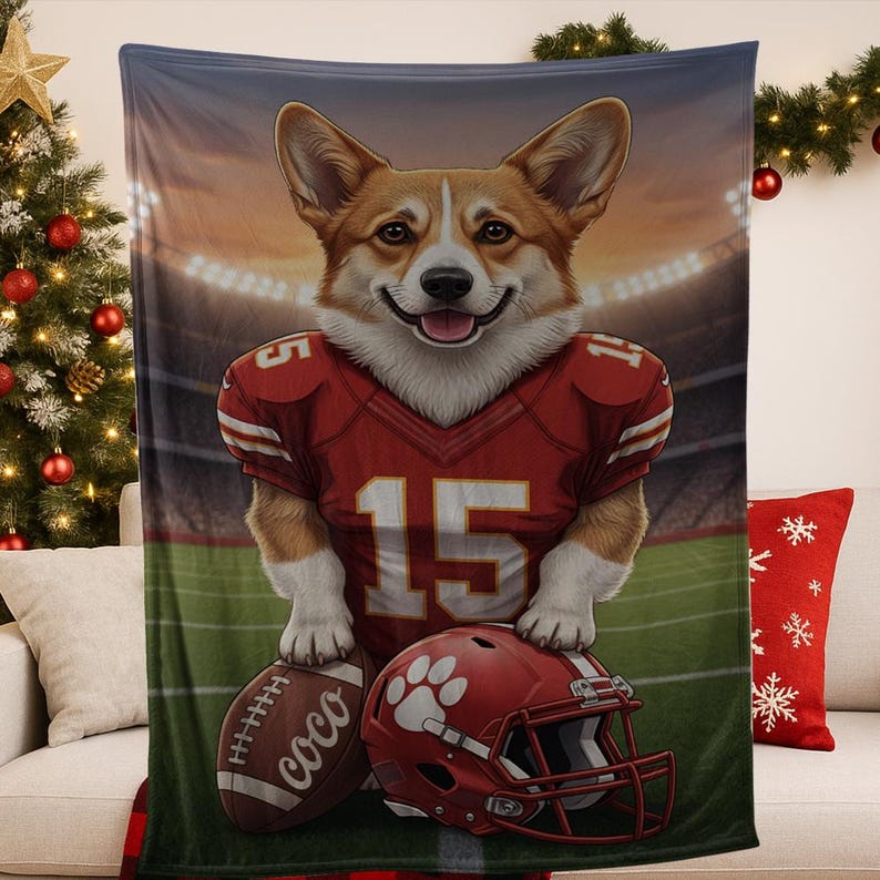 Puede incluir: Una manta con un corgi sonriente que lleva una camiseta de f&uacute;tbol roja con el n&uacute;mero 15. La manta tambi&eacute;n muestra un bal&oacute;n de f&uacute;tbol y un casco rojos. El bal&oacute;n tiene el nombre "coco". El fondo representa un estadio de f&uacute;tbol.