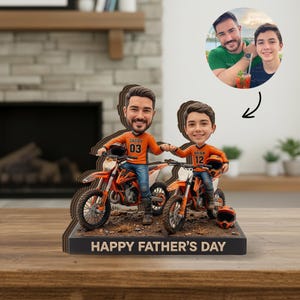 May include: A custom bobblehead figurine set featuring two figures on orange dirt bikes, one labeled DADDY 03 and the other BRIAN 12, mounted on a black base with the text HAPPY FATHER'S DAY. A circular inset shows the original reference photo.