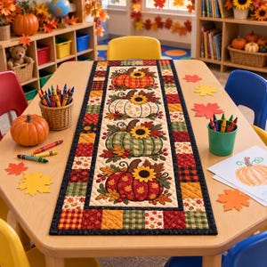 May include: A rectangular table runner featuring a central panel with four stacked pumpkins, each topped with a sunflower, surrounded by a border of colorful autumn-themed patchwork squares in shades of orange, red, yellow, and green.