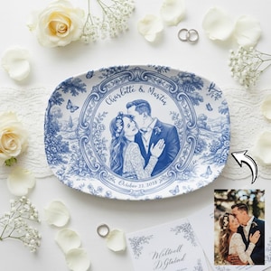 Könnte beinhalten: Eine ovale, blau-weiße dekorative Platte mit einem Paarporträt, umgeben von einem floralen und landschaftlichen Design. Die Platte enthält die Namen "Charlotte & Martin" und das Datum "22. Oktober 2025".