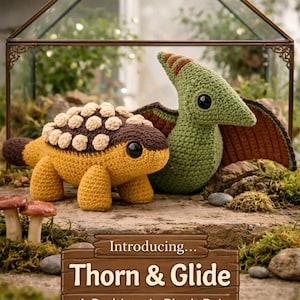 May include: A pair of handmade crochet plush dinosaurs, a yellow and brown ankylosaurus and a green pterodactyl, are displayed on a stone surface. The sign reads "Introducing... Thorn & Glide A Prehistoric Plush Pair."