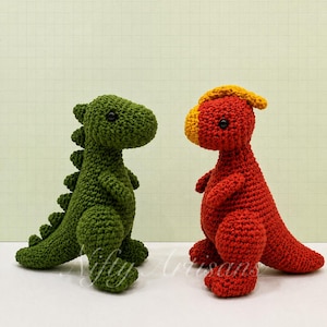 May include: Two crocheted dinosaur toys standing side by side. The left dinosaur is dark green with a row of spikes along its back. The right dinosaur is red with a yellow snout and crest. Both have black bead eyes and a textured yarn finish.