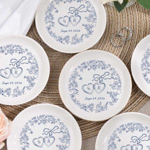 May include: White ceramic plates with a blue floral design border. Each plate features two connected heart shapes with the letters "S" and "R" inside, and the date "Sept 09.2026".