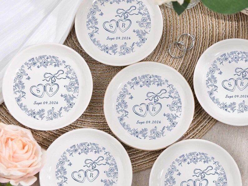 May include: White ceramic plates with a blue floral design border. Each plate features two connected heart shapes with the letters "S" and "R" inside, and the date "Sept 09.2026".