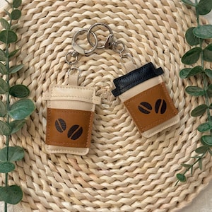 Puede incluir: Dos llaveros con forma de taza de caf&eacute;. Un llavero es de color beige y marr&oacute;n con detalles de granos de caf&eacute; negros. El otro llavero es negro y marr&oacute;n con detalles de granos de caf&eacute; negros. Ambos tienen llaveros plateados.