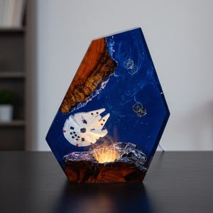 Peut inclure: Lampe géométrique unique représentant le vaisseau spatial Millennium Falcon dans un décor en résine bleue et marron. La lampe émet une lumière chaude et brillante depuis sa base, créant un affichage captivant. La lampe mesure environ 20 cm de haut.