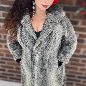 May include: A woman wearing a gray faux fur coat with a red ear warmer. She is standing in front of a brick wall.