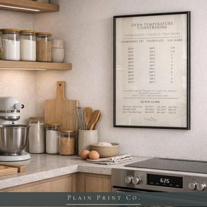 Op de afbeelding: Een ingelijste wandprint met een oven-temperatuurconversietabel met Fahrenheit-, Celsius- en Gas Mark-waarden. De tekst bevat een beknopte handleiding voor oveninstellingen, gedrukt in zwart op een lichte cr&egrave;mekleurige achtergrond.