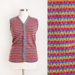 May include: A sleeveless, button-down vest with a colorful striped pattern. The vest features a V-neck and is displayed on a mannequin. The color scheme includes pink, yellow, blue, and gray. The fabric has a textured appearance.