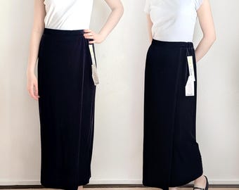 May include: A long, dark navy blue wrap skirt. The skirt is made of a soft, velvet-like material and has a wrap design. The skirt is paired with a white t-shirt and black flats. A tag is attached to the skirt.