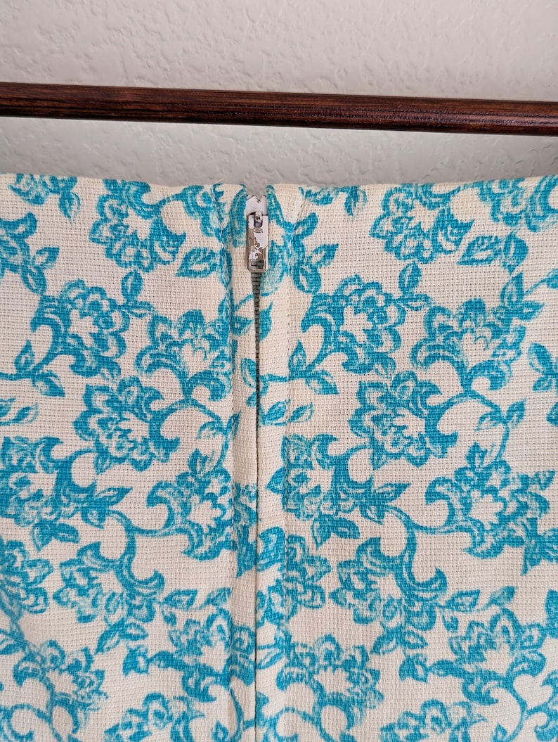 Pu&ograve; includere: Un vestito bianco con motivo floreale blu e chiusura a zip sul retro.