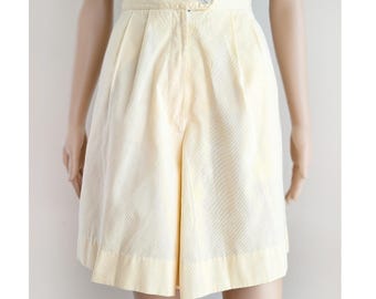 May include: Pale yellow shorts with a button closure and pleats. The shorts have a high waist and a tailored fit. The fabric appears to be a lightweight material, suitable for warm weather. The shorts are a solid color with a simple, classic design.