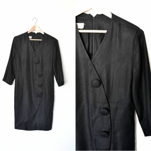 May include: A black, long-sleeved dress with a wrap-style neckline and a row of large, black buttons down the side.
