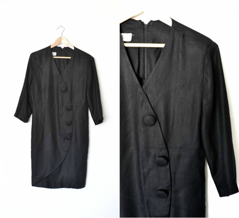 May include: A black, long-sleeved dress with a wrap-style neckline and a row of large, black buttons down the side.