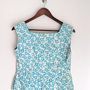 Pu&ograve; includere: Un top bianco senza maniche con un motivo floreale blu. Il top ha una scollatura quadrata e una chiusura a zip sul retro.