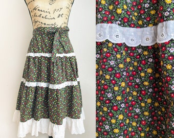 May include: A green, red and yellow floral print skirt with white lace trim. The skirt has a tiered design and is made of a lightweight fabric.