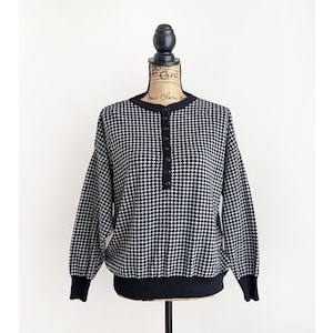 May include: Black and white patterned sweater with a button-up neckline and long sleeves. The sweater has a houndstooth design and black ribbed cuffs and hem. The garment is displayed on a mannequin.