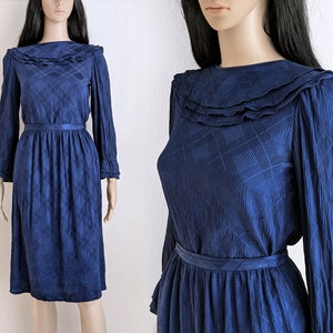 May include: A vintage navy blue dress with a ruffled collar and long sleeves. The dress features a subtle diamond pattern and a matching belt at the waist. The dress is knee-length and has a classic, elegant style.