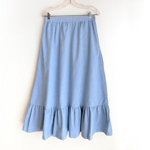May include: A light blue denim skirt with a ruffled hem. The skirt has a simple design and is a classic style.