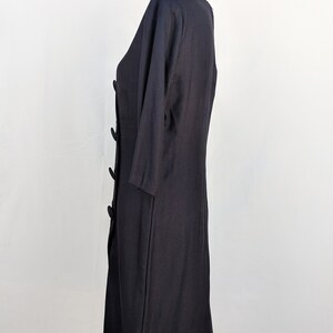May include: A black dress with a round neckline and three-quarter sleeves. The dress has a button closure and a fitted silhouette.