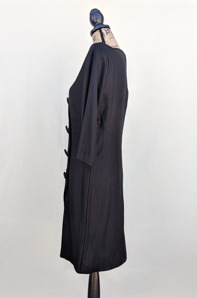 May include: A black dress with a round neckline and three-quarter sleeves. The dress has a button closure and a fitted silhouette.