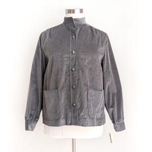 May include: A gray corduroy shirt with a stand-up collar and button closure. The shirt has two patch pockets on the front and long sleeves.
