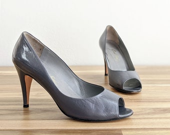 May include: A pair of gray peep-toe heels with a stiletto heel. The shoes are made of leather and have a pointed toe.