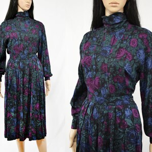 Puede incluir: Un vestido negro de manga larga con cuello alto y estampado floral con rosas moradas, azules y verdes. El vestido tiene una falda plisada.