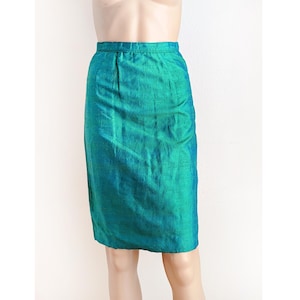 Op de afbeelding: Een turquoise potloodrok. De rok is gemaakt van een glinsterende stof die licht reflecteert, waardoor een gradiënteffect van turquoise en groene tinten ontstaat. De rok heeft een klassiek, getailleerd ontwerp met een getailleerde taille en een rechte silhouet.