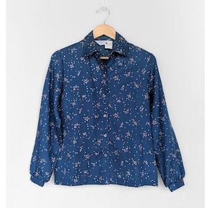 Op de afbeelding: Een blauw overhemd met lange mouwen, een witte kraag en een klein bloemenprintje.