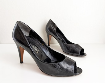 May include: A pair of black leather peep-toe heels with a stiletto heel. The shoes have a textured leather upper and the brand name "Martini" is printed on the insole.