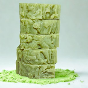 May include: A stack of five green soap bars with a swirl pattern on a bed of green powder.