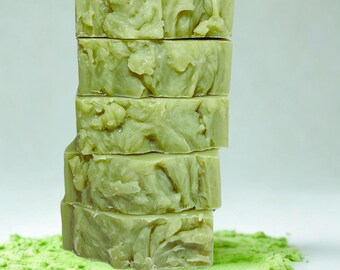 May include: A stack of five green soap bars with a swirl pattern on a bed of green powder.