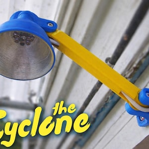 Puede incluir: Una lámpara ajustable azul y amarilla con el texto "the Cyclone" en amarillo. La lámpara tiene una pantalla y base azules, con un brazo amarillo. Está montada en una pared.