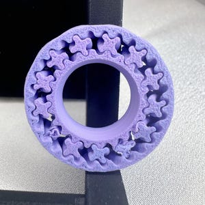 Peut inclure: Gros plan sur un engrenage imprimé en 3D de couleur violette avec un motif en forme d'étoile. L'engrenage est en plastique et a une finition lisse.