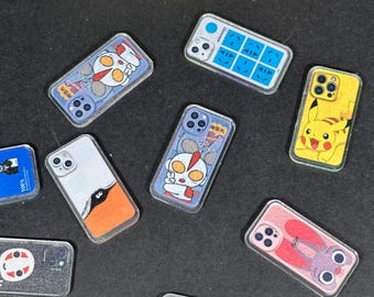 May include: A collection of clear phone cases with various designs. The cases feature cartoon characters, patterns, and a NASA logo. Colors include blue, yellow, pink, and white. The cases are rectangular and have camera cutouts.