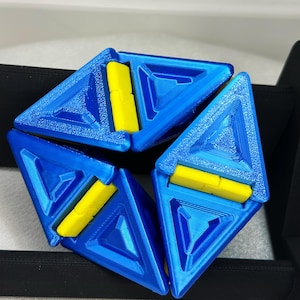 May include: A blue and yellow geometric puzzle with six triangular pieces that fit together. The puzzle is made of plastic and has a textured surface.