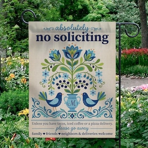 May include: A beige garden flag with the words "absolutely no soliciting" in blue script. The flag features a floral design with blue birds and a vase with the letter "M". The bottom text reads "Unless you have tacos, iced coffee or a pizza delivery. please go away."