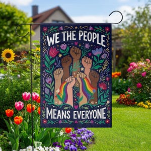Könnte beinhalten: Eine marineblaue Gartenflagge mit dem Text "WE THE PEOPLE MEANS EVERYONE" und Illustrationen von erhobenen Fäusten in verschiedenen Hauttönen und einem Regenbogen. Die Flagge ist von floralen Designs umgeben.