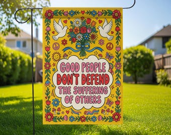 Könnte beinhalten: Eine gelbe Gartenflagge mit dem Text "GOOD PEOPLE DON'T DEFEND THE SUFFERING OF OTHERS" in einer Retro-Schriftart. Die Flagge zeigt ein Blumen- und Taubendesign mit einem blauen Band. Die Flagge wird auf einem schwarzen Metallständer in einem grasbewachsenen Garten gezeigt.