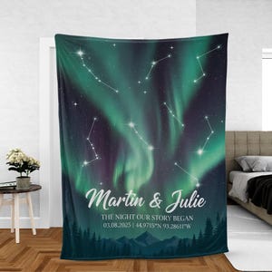 May include: A personalized blanket featuring a celestial design with constellations and an aurora borealis effect in shades of green and purple. The blanket includes the names "Martin & Julie", date, and coordinates.