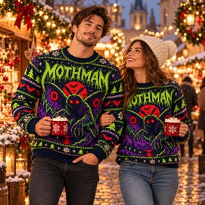 May include: Two matching navy blue knit sweaters featuring a large Mothman graphic with glowing red eyes, a red moon, and green text. The sweaters have a festive pattern of small green trees, red bats, and white snowflakes against a dark background.