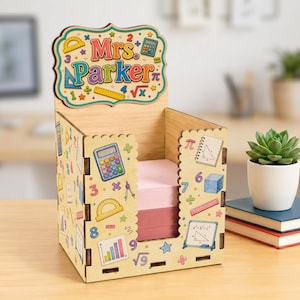 May include: A light-colored wooden desk organizer featuring a scalloped top sign that reads Mrs. Parker. The sides are decorated with colorful math-themed graphics including calculators, rulers, geometric shapes, and numbers, holding a stack of paper.