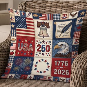 Pode incluir: Almofada decorativa quadrada com um design de patchwork com símbolos patrióticos. A almofada inclui a bandeira americana, o Sino da Liberdade, uma águia e os textos "USA 250" e "1776 2026". O esquema de cores é vermelho, branco e azul.