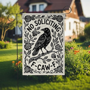 K&ouml;nnte beinhalten: Eine rechteckige Gartenflagge mit einem schwarz-wei&szlig;en Design. Die Flagge zeigt eine Kr&auml;he auf einem Ast, umgeben von Rosen und den Worten "NO SOLICITING" und "F-CAW-F". Die Flagge wird auf einem schwarzen Metallst&auml;nder in einem Garten gezeigt.