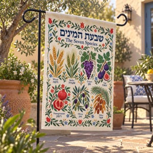 May include: A rectangular garden flag featuring a cream-colored background with a decorative floral border. The text reads "The Seven Species" and "שבעת המינים" above illustrations of wheat, barley, grapes, figs, pomegranates, olives, and dates with labels.