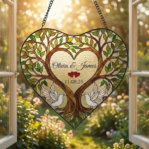 May include: Heart-shaped stained glass art piece with a tree design, two doves, and the names "Olivia & James" with a date. The artwork features brown, green, and gold tones, and is suspended by a black chain.